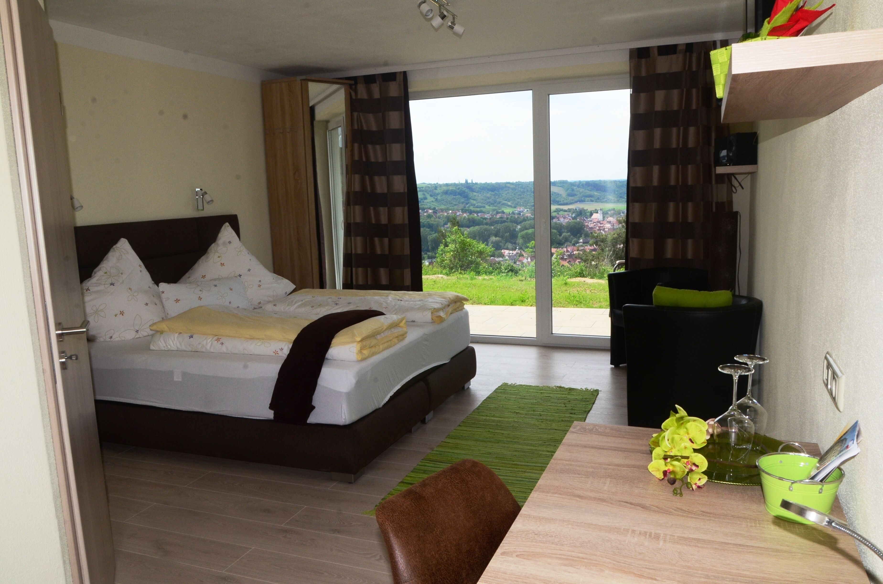 Ein Schlafzimmer mit einem Bett, einem Schreibtisch mit Stuhl, einem grünen Teppich und Blick auf eine grüne Landschaft durch ein Fenster.