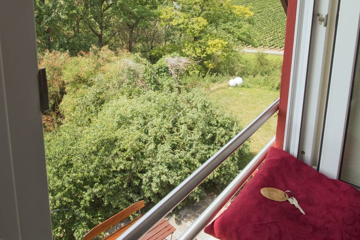 A balcony with a red cushion and keys, overlooking a lush green landscape with trees and a distant view of a town.