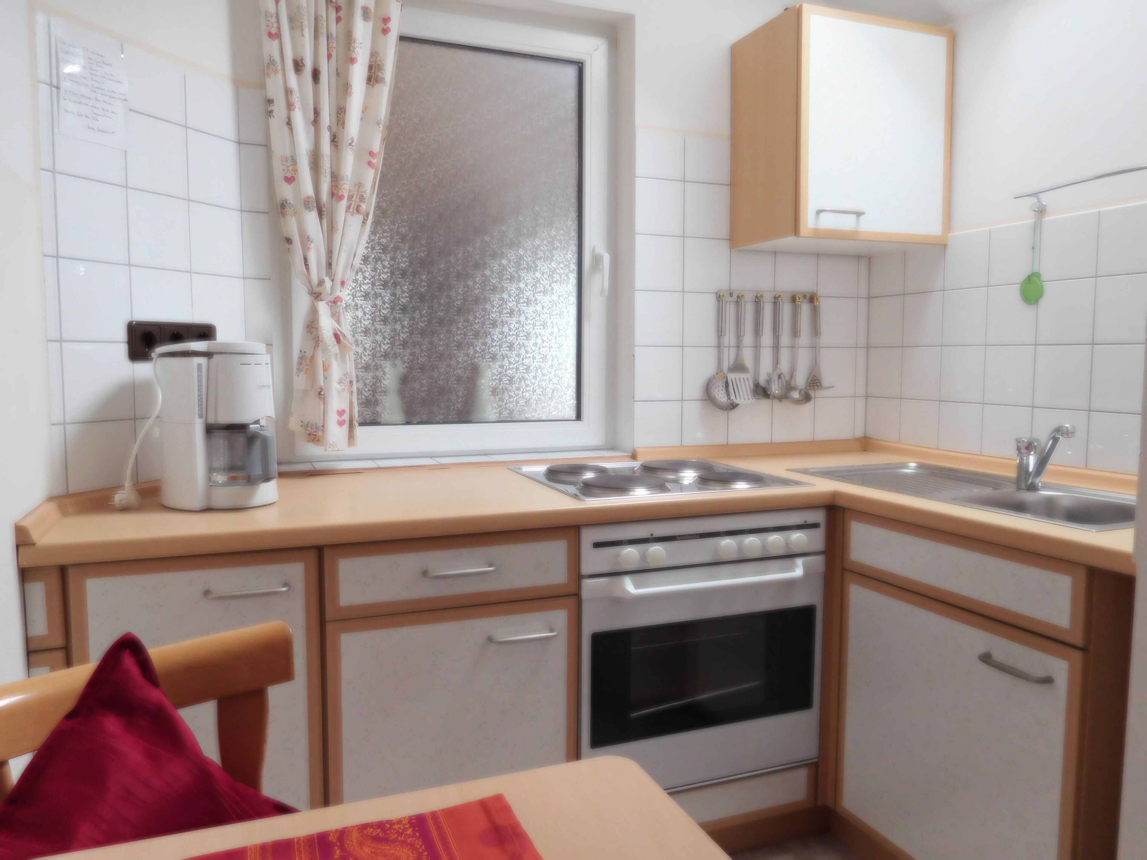 A compact kitchen with a coffee maker, a stove, an oven, a sink, and a window with curtains.
