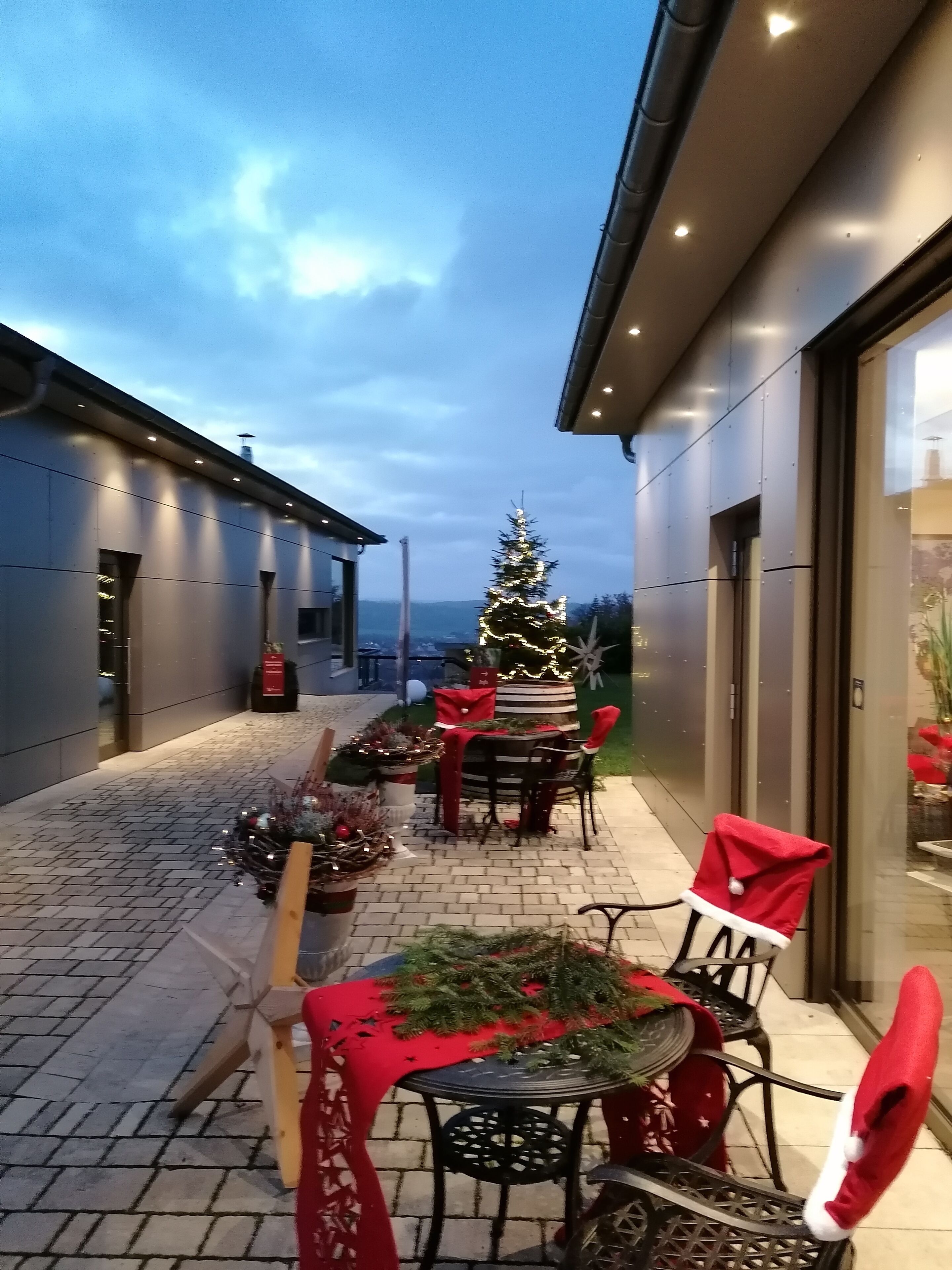 A paved outdoor area with a Christmas tree, tables, and chairs decorated with red and white.