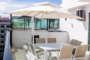 En tagterrasse med et bord, stole og en stor parasol, samt en pool i baggrunden.