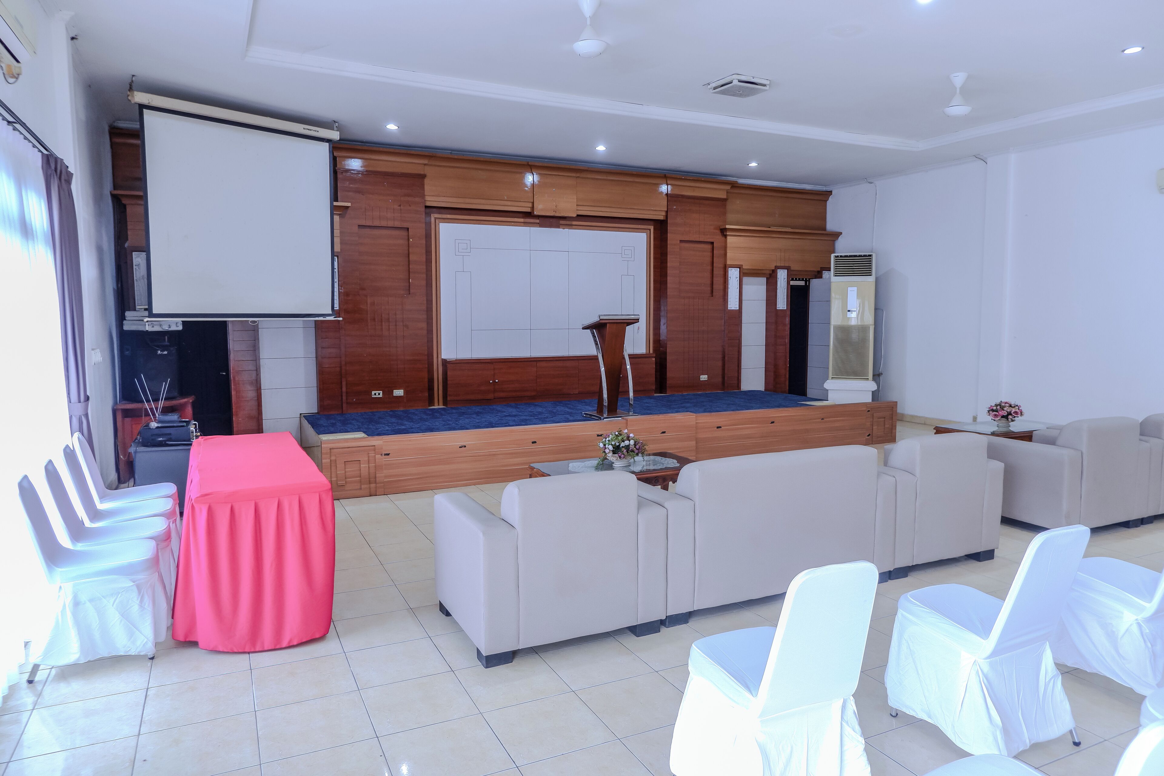 A spacious living area with a large sofa set, a coffee table, and a small stage with a podium.