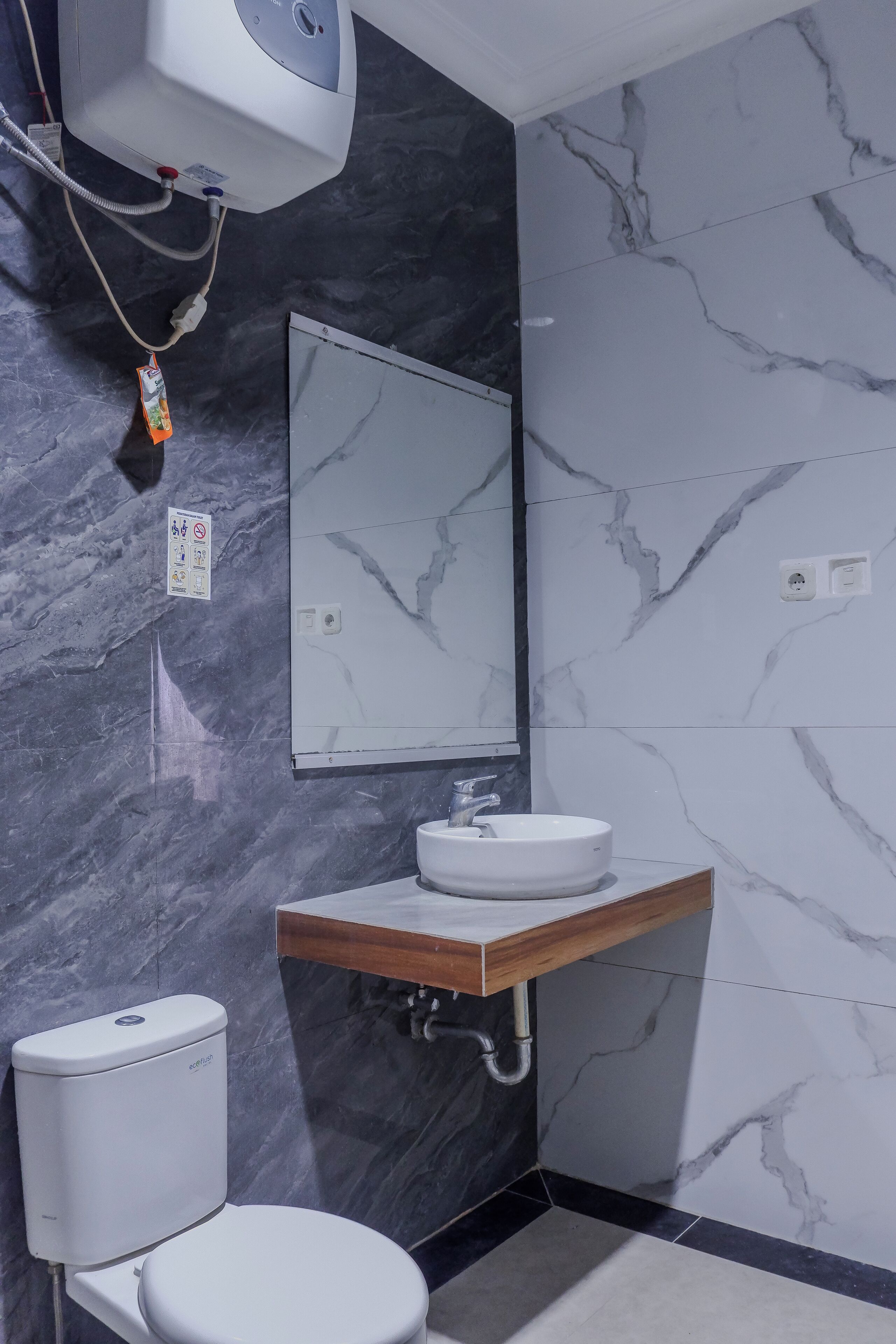 A modern bathroom with a marble backsplash, a white toilet, a wooden vanity with a sink, and a wall-mounted mirror.