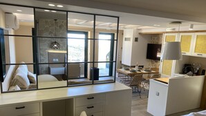 Een moderne hotelkamer met een grote spiegel, een zithoek met een tafel gedekt voor twee personen, en een gezellige zithoek met een bank en een stoel.