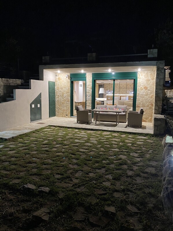 Un patio moderno al aire libre con paredes de piedra y puertas verdes, que incluye una zona de comedor con sillas y una mesa.