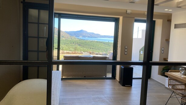 Een moderne kamer met een groot raam met uitzicht op een bergachtig landschap en een wateroppervlak.