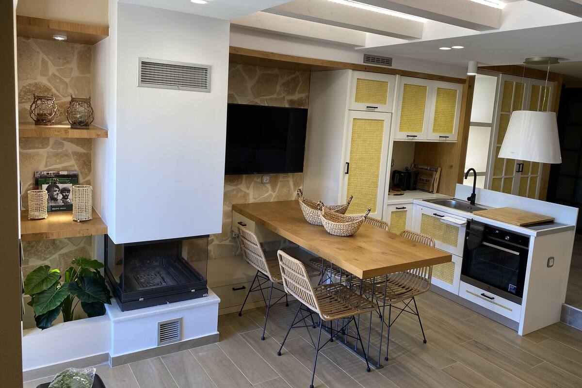 A modern kitchen with a wooden table, wicker chairs, and built-in appliances.