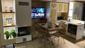 Een moderne keuken met een eethoek, een televisie waarop een film draait, en een stenen muur.
