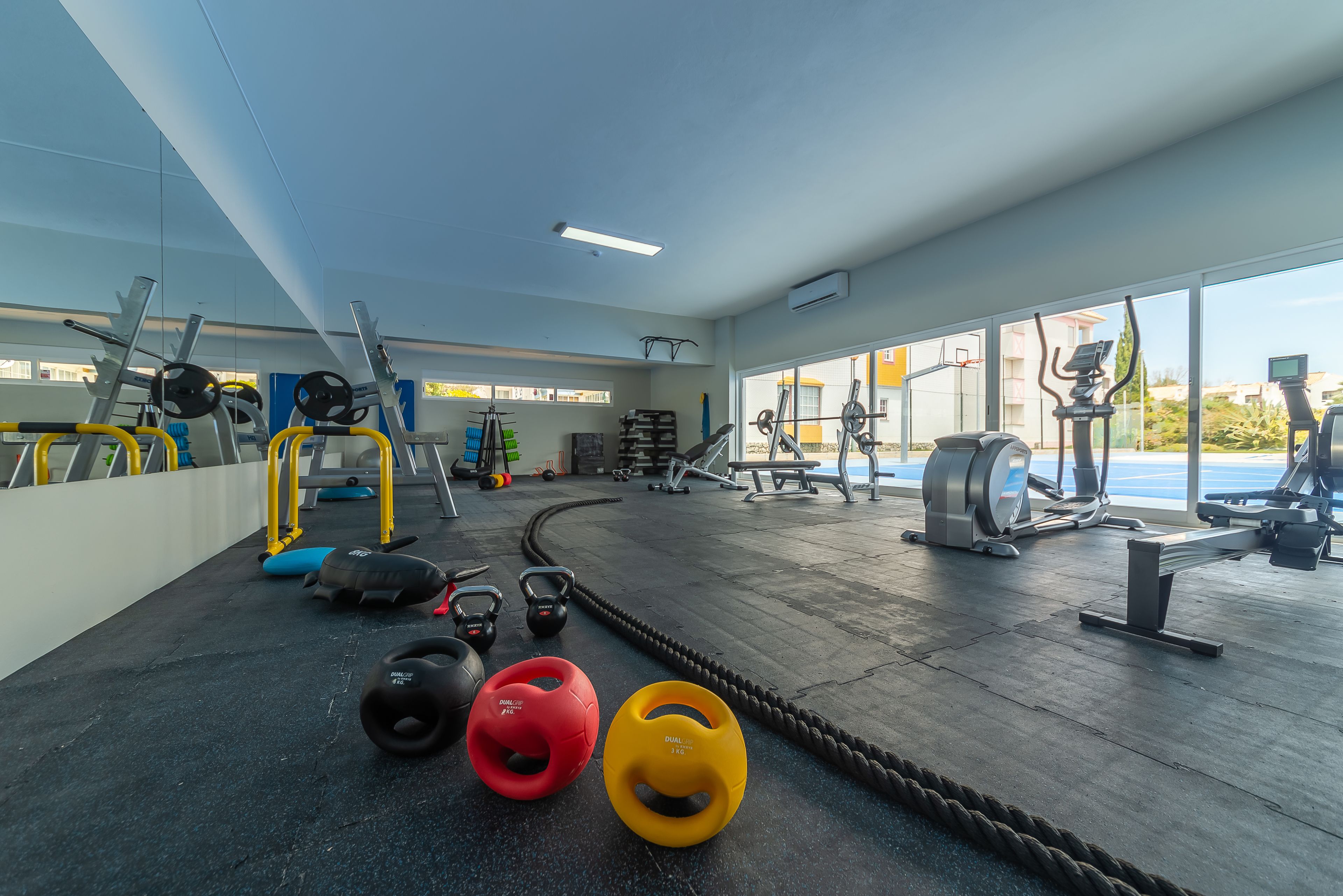 Ein Fitnessstudio mit unterschiedlichen Trainingsgeräten, darunter Kettlebells, ein Rudergerät und ein Ergometer.