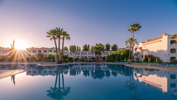 A resort pool with clear reflections, palm trees, and a building with multiple balconies. - Golden Club Cabanas (Tavira)