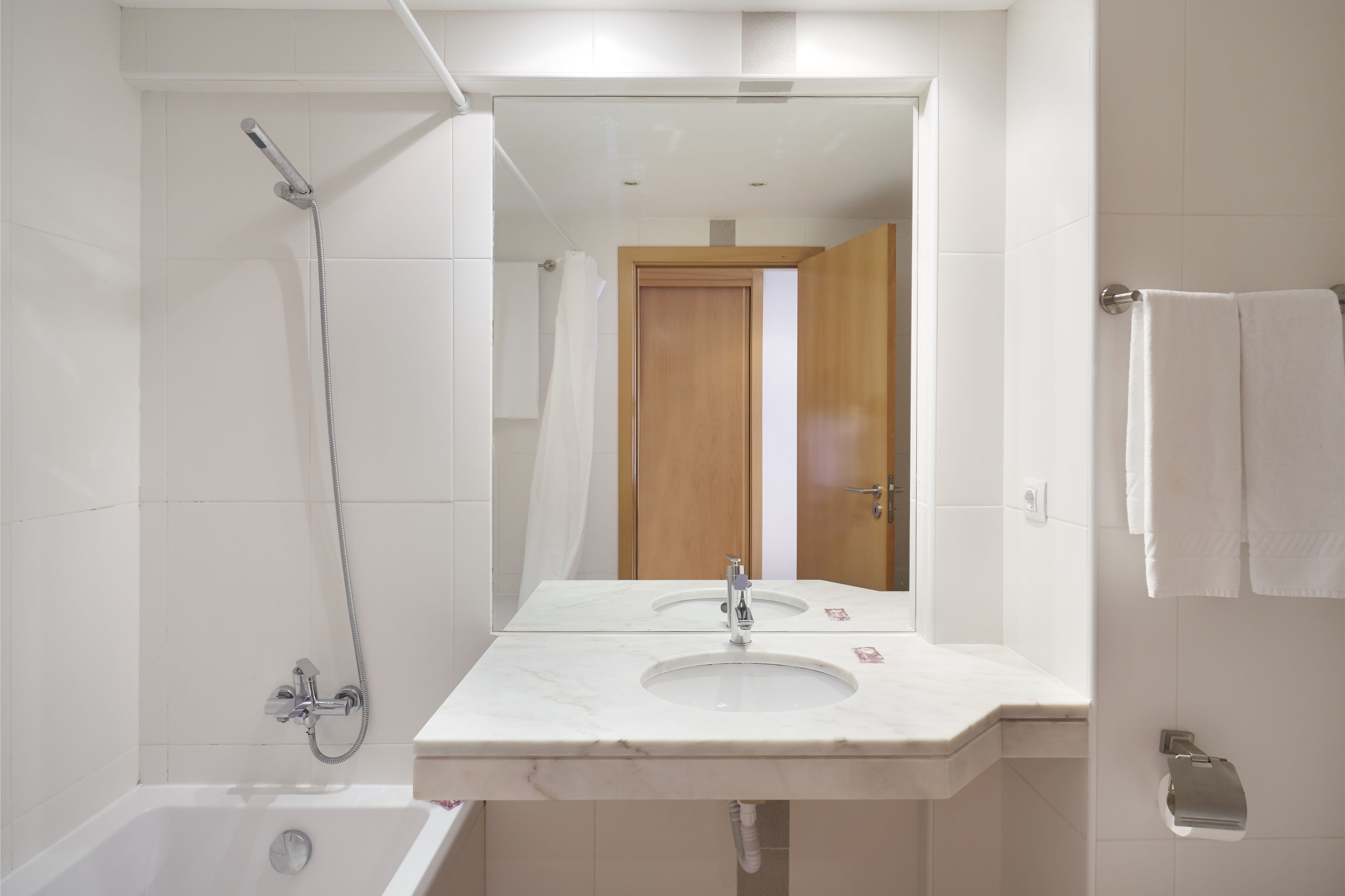 A modern bathroom with a white sink, a shower, and a wooden door.
