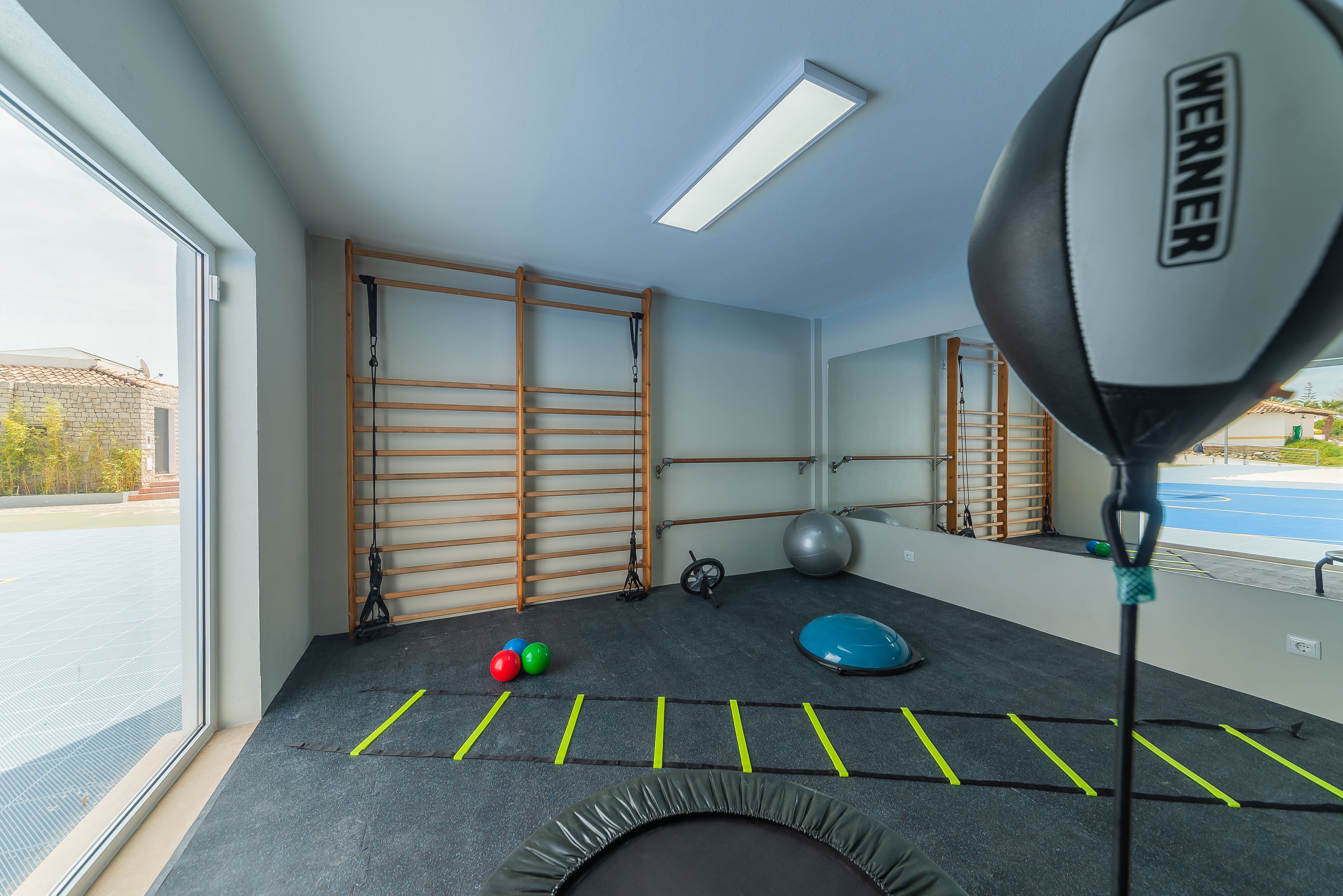 Une salle de sport équipée de matériel d’exercice, d’un trampoline et d’une fenêtre donnant sur une cour.