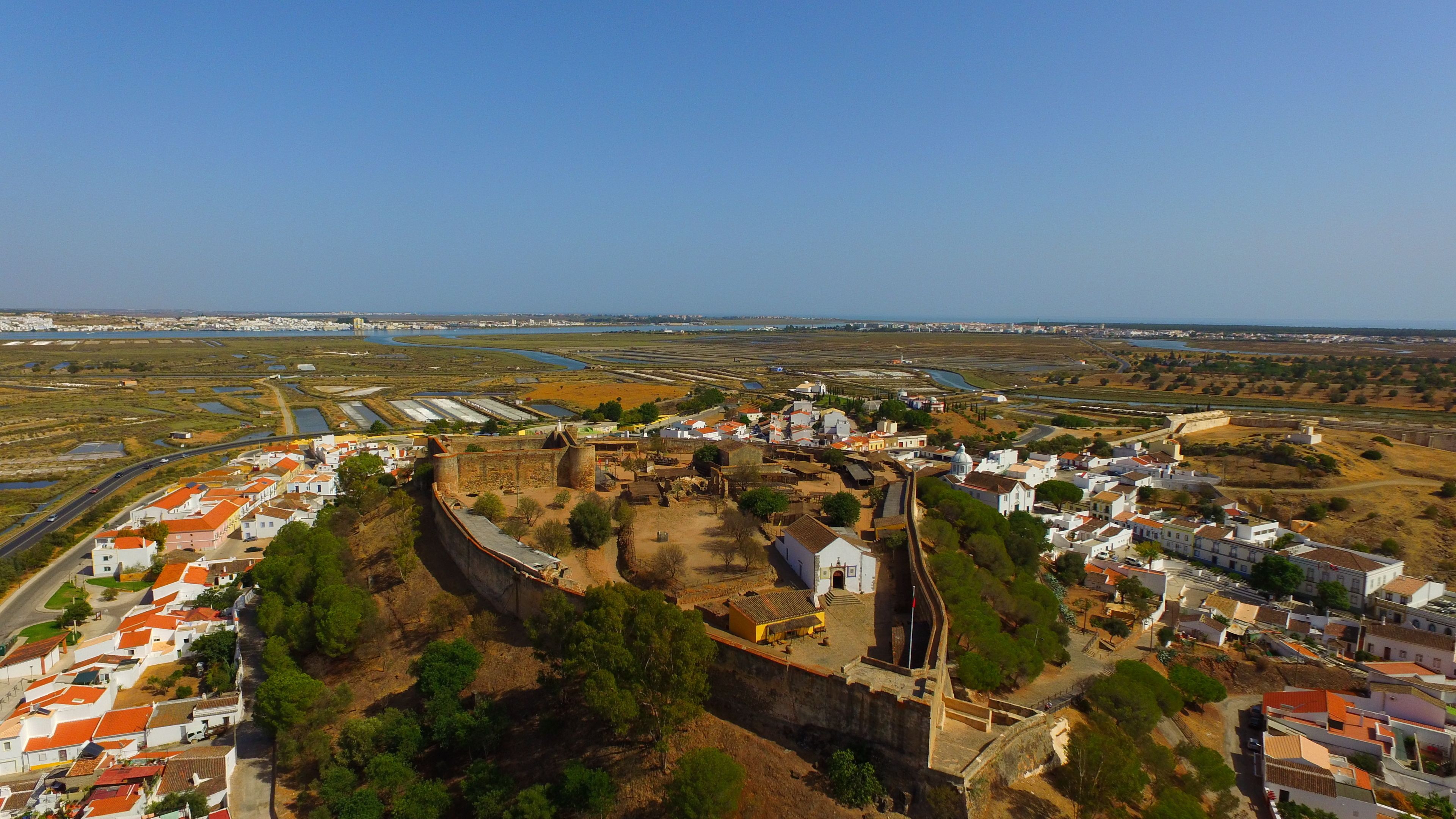 A coastal town with a historic fort, white buildings with red roofs, and a clear view of the sea.