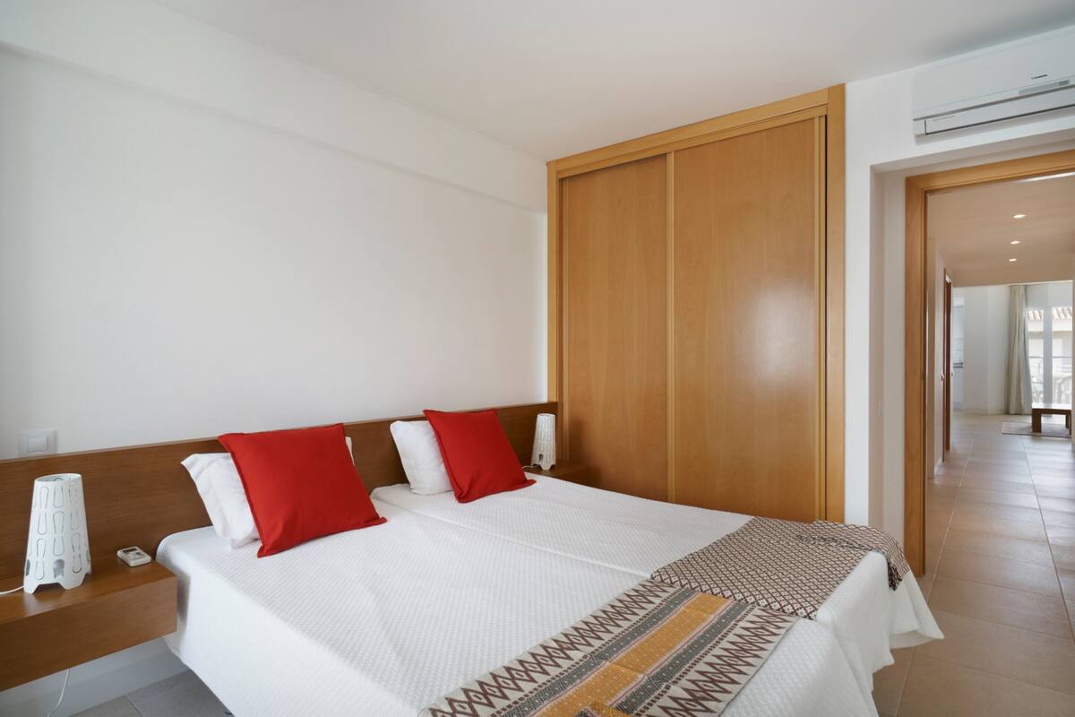 A hotel room with a large bed, wooden wardrobe, and a bedside table with a lamp.