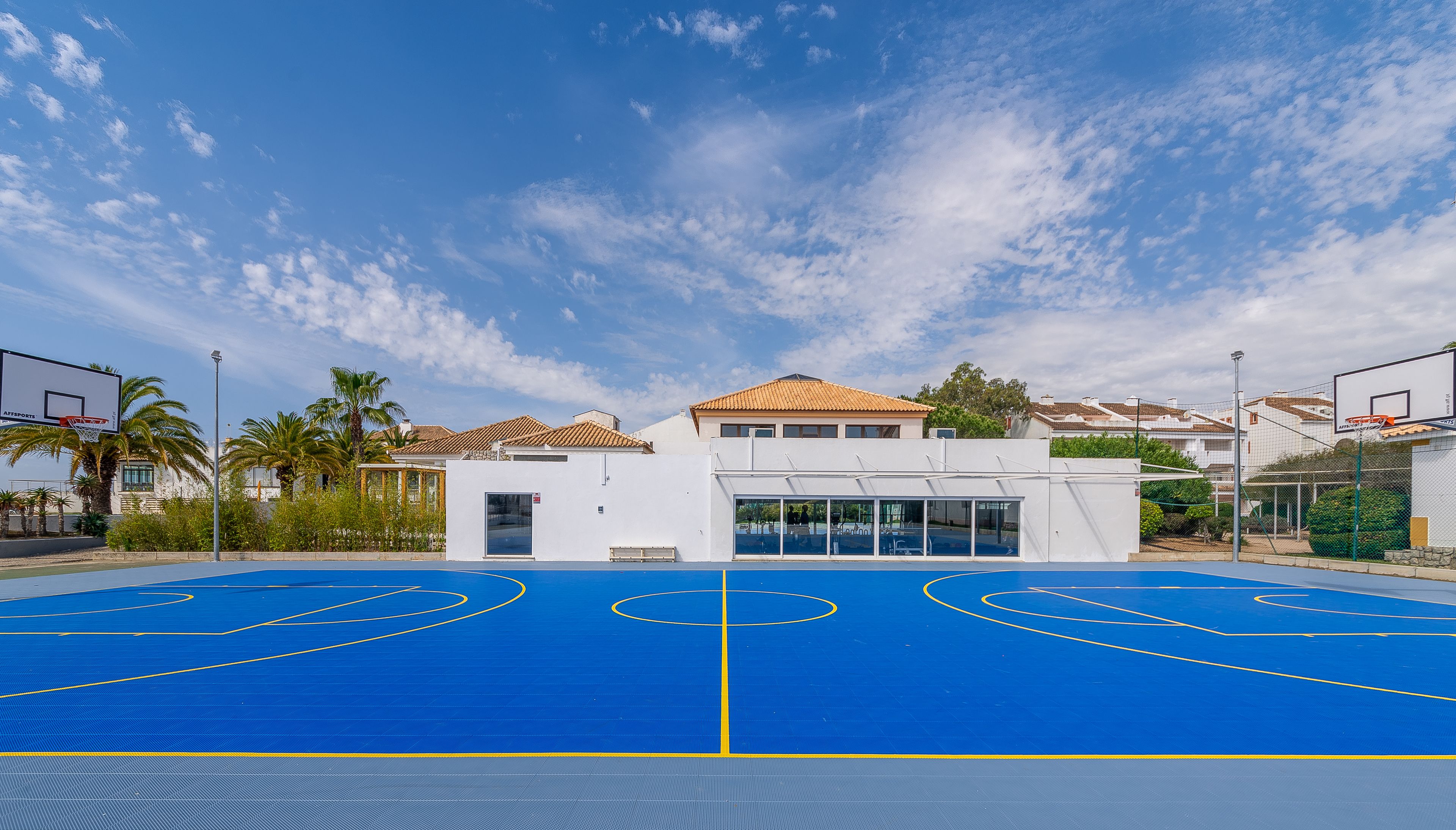 Una cancha de baloncesto al aire libre con un edificio blanco al fondo.