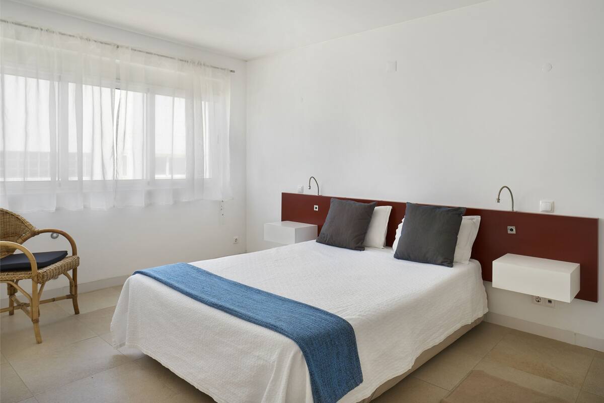 A neatly made bed with a white and blue bedspread, a wooden headboard, and a bedside table with a lamp.