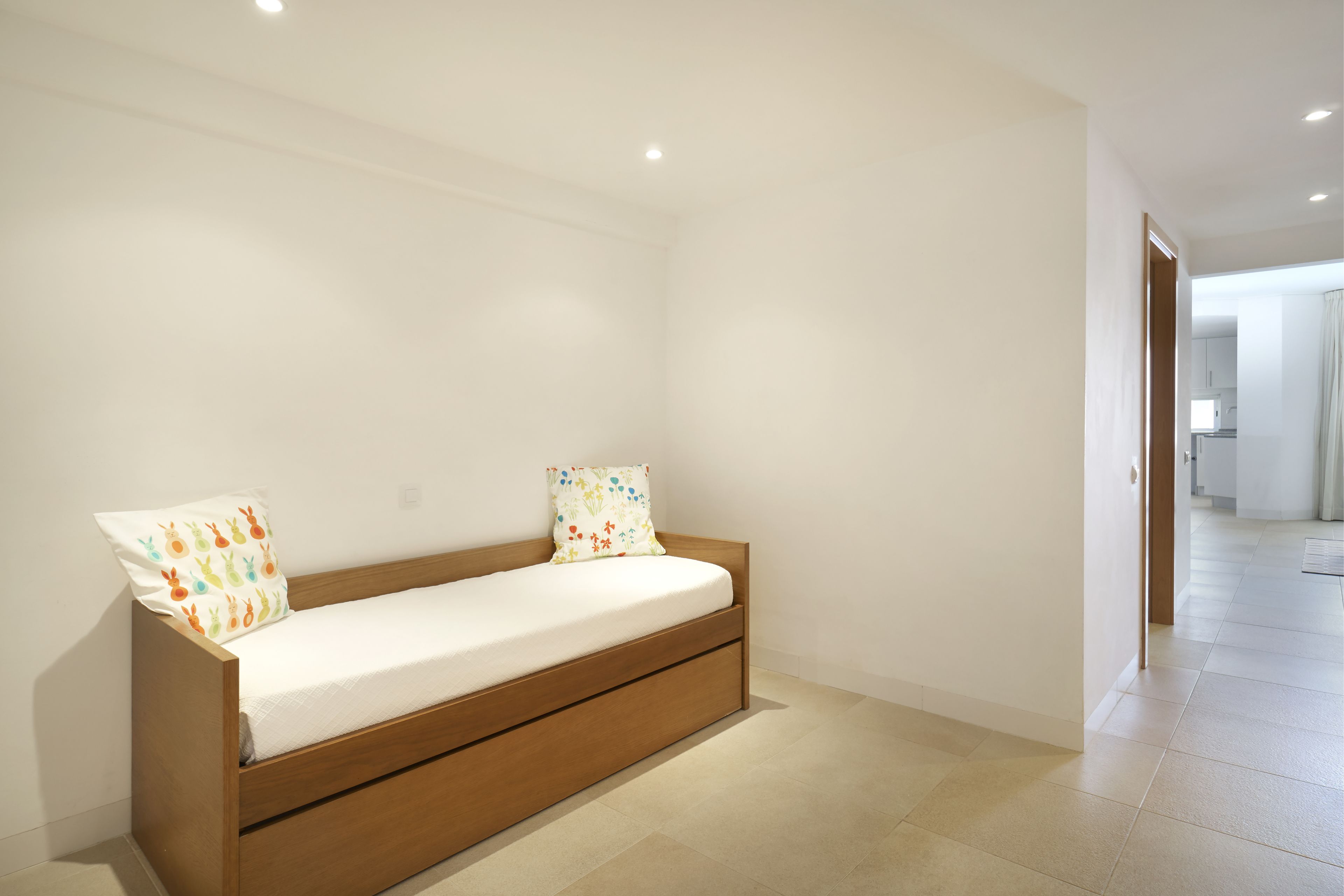 Een minimalistische kamer met een bed van hout, witte wanden en een betegelde vloer.