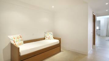 Een minimalistische kamer met een bed van hout, witte wanden en een betegelde vloer.