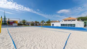 Una cancha de voleibol de playa con arena y superficie azul, rodeada de edificios y palmeras.
