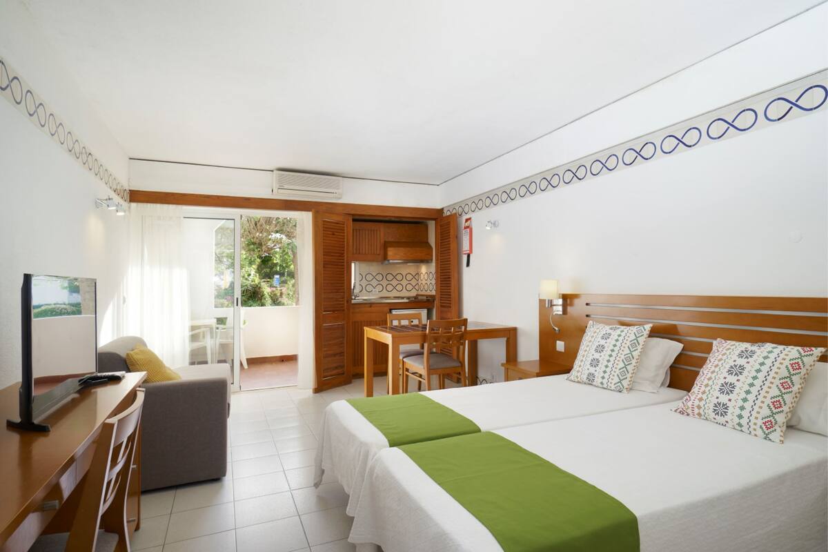 A hotel room with a bed, a desk, a chair, a small table, and a kitchenette.