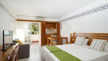 A hotel room with a bed, a desk, a chair, a small table, and a kitchenette.