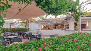 An outdoor seating area with tables and chairs, a bar, and a garden with pink flowers. - Golden Club Cabanas (Tavira)