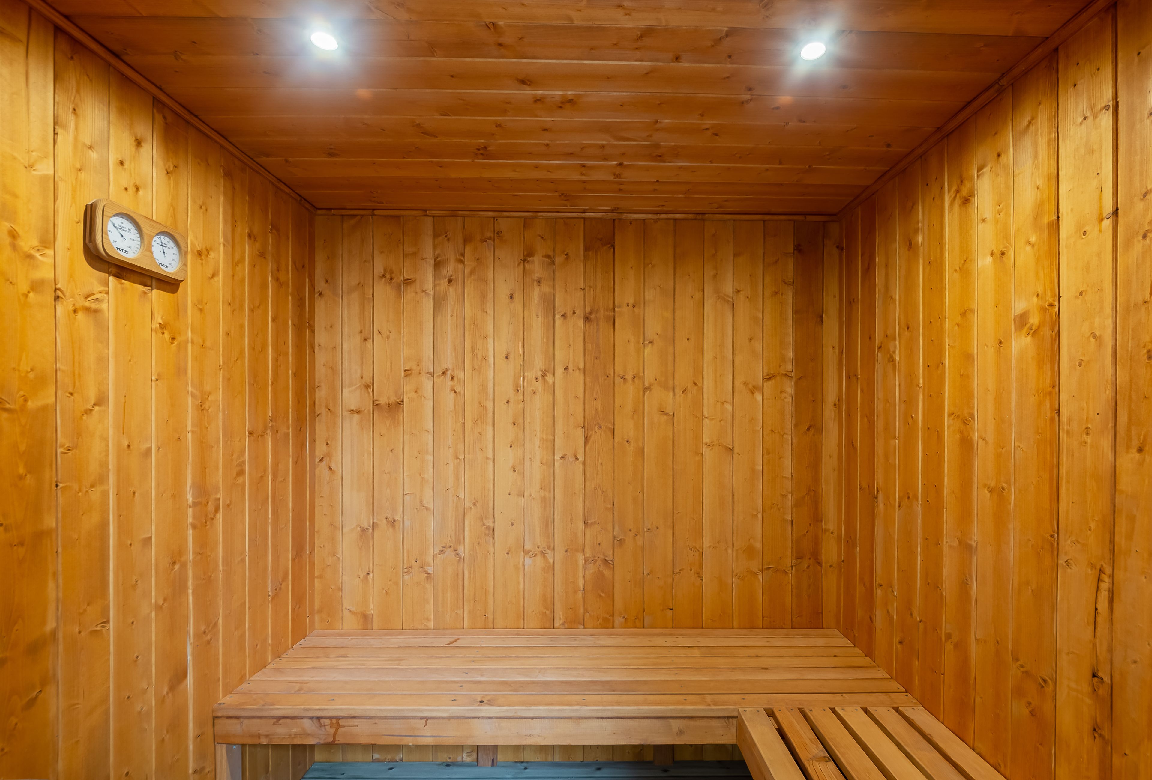 Een houten sauna met een bank, houten wanden en twee wandklokken.