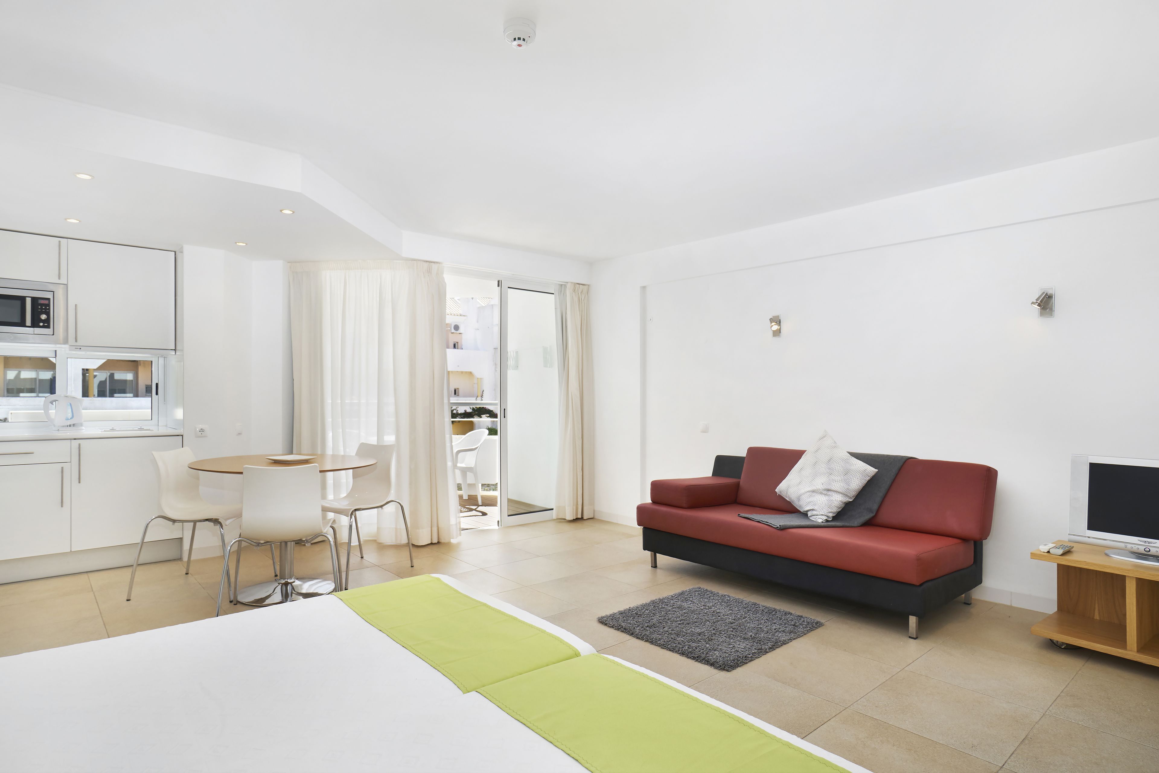 Une chambre d’hôtel moderne, équipée d’un lit, d’un canapé rouge, d’une télévision et d’un coin repas avec une table et des chaises.