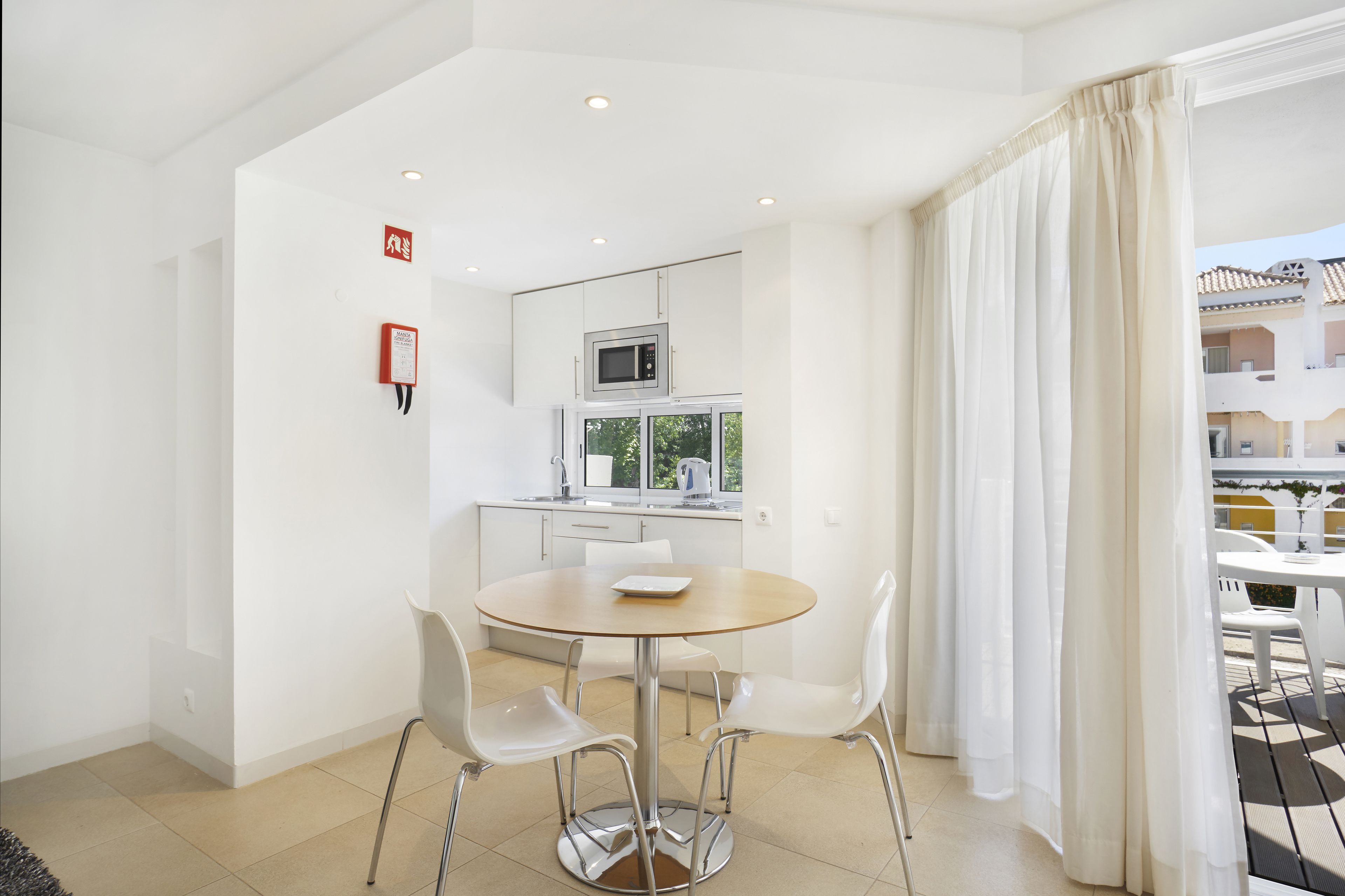 A modern kitchen with white cabinets, a microwave, and a window. There is a round table with chairs in the foreground.