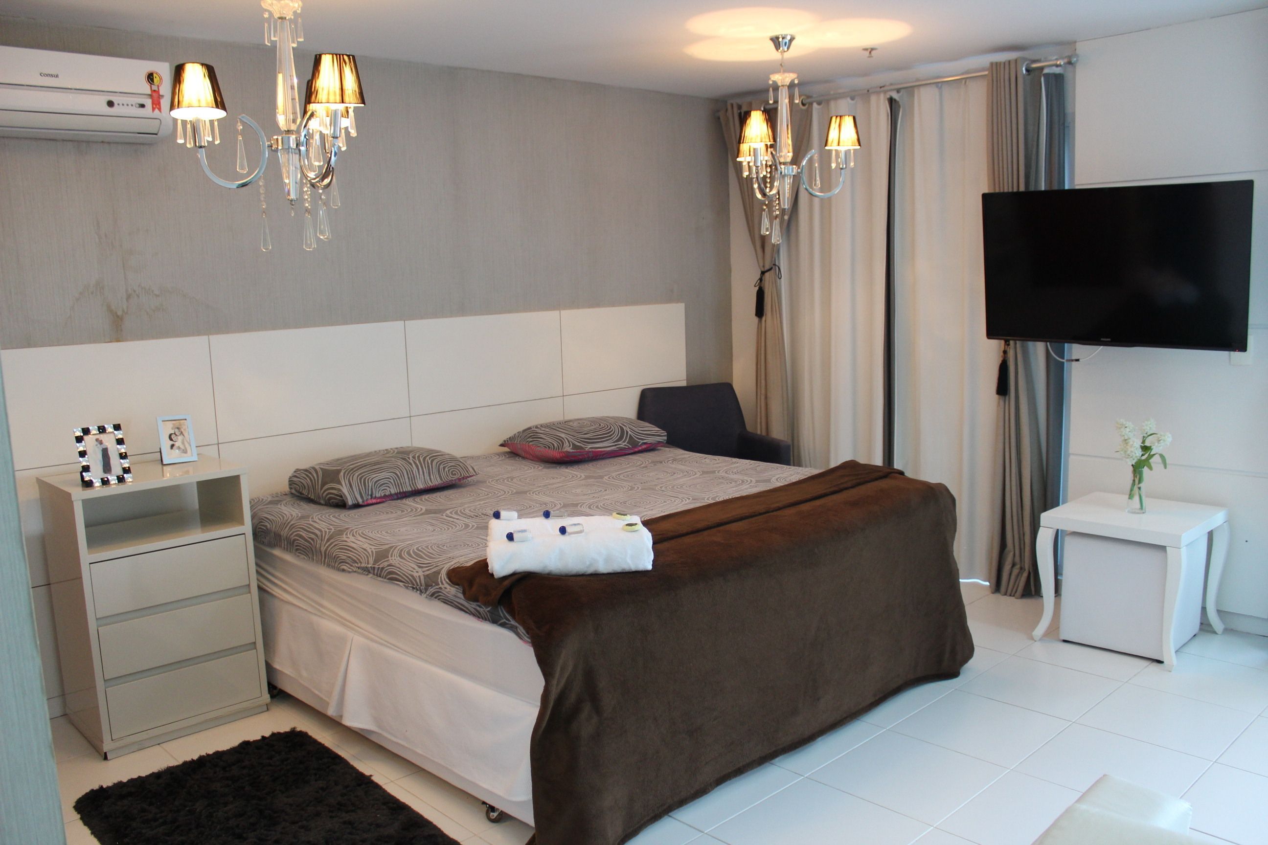 Een moderne slaapkamer met een groot bed, nachtkastjes, een televisie en een kroonluchter.