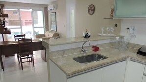 Cocina moderna con encimera de granito, pileta de acero inoxidable y muebles blancos. Cuenta con un comedor con mesa y sillas de madera, y una ventana que proporciona luz natural.