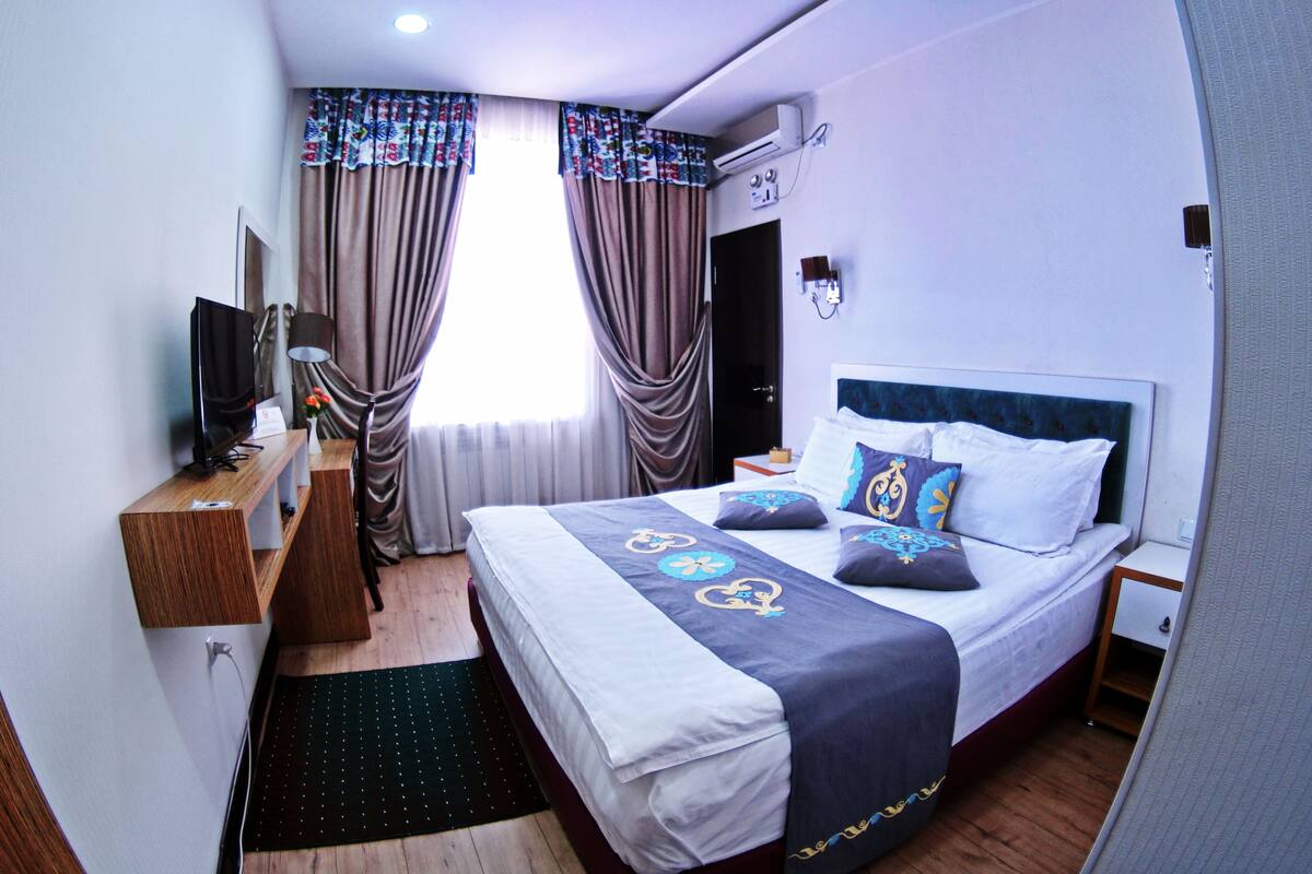 Une chambre d’hôtel avec un lit, un bureau, une télévision et des rideaux.