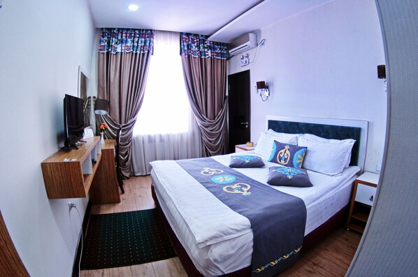A hotel room with a bed, a desk, a TV, and curtains.