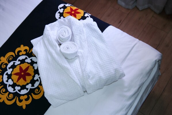 A neatly made bed with white linens and a decorative bedspread with floral patterns. - Rohat Hotel (Dushanbe)