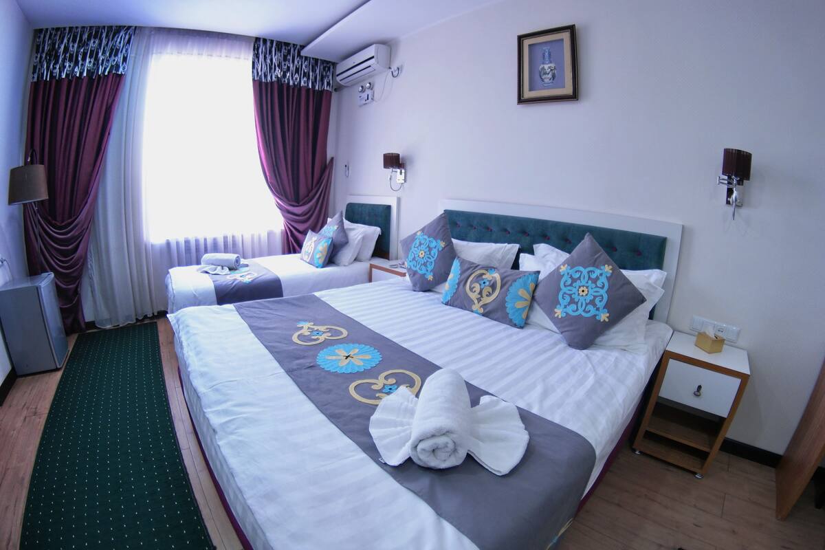 Une chambre d’hôtel avec deux lits, un tapis vert, une table de chevet avec une lampe et un climatiseur fixé au mur.