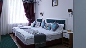 Ein Hotelzimmer mit zwei Betten, einem großen Fenster mit durchsichtigen Vorhängen, einer Klimaanlage, einem gerahmten Bild an der Wand und einem Nachttisch mit Lampe.