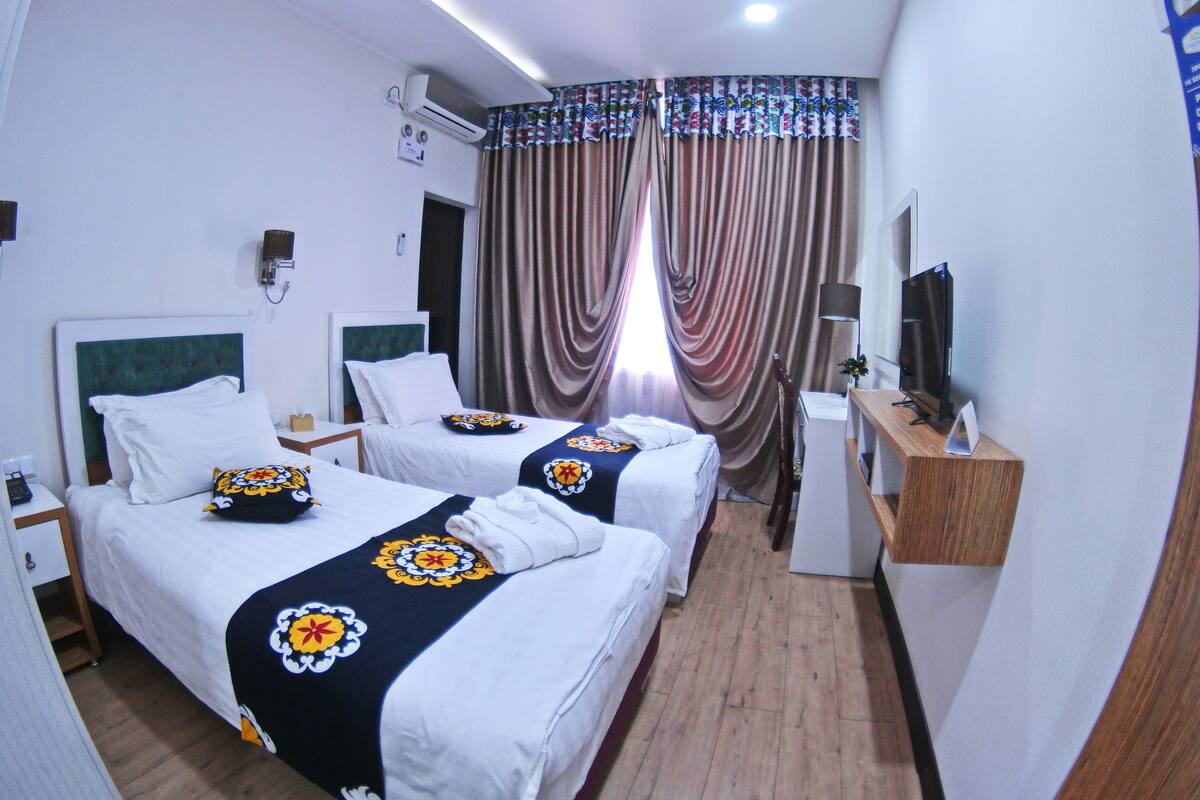 Une chambre d’hôtel avec deux lits, une télévision, un bureau et une fenêtre avec des rideaux.