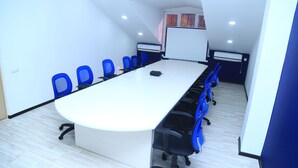 Ein Konferenzraum mit einem langen Tisch, blauen Stühlen und einer Whiteboard-Wand.