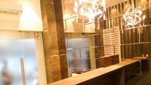 A modern bathroom with a marble wall, a wooden vanity, a mirror, and a chandelier. - The Fountain Inn - Fort (Mumbai)