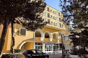 Ein mehrstöckiges Gebäude mit gelber Fassade, gewölbten Fenstern und einem Auto davor.
