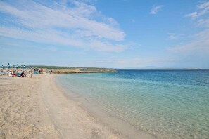 Ein Strand mit klarem, flachem Wasser, einem Sandufer und einem fernen Horizont.
