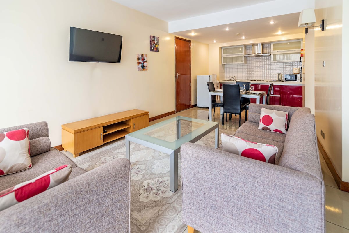 A living room with a sofa, a glass coffee table, and a TV mounted on the wall.