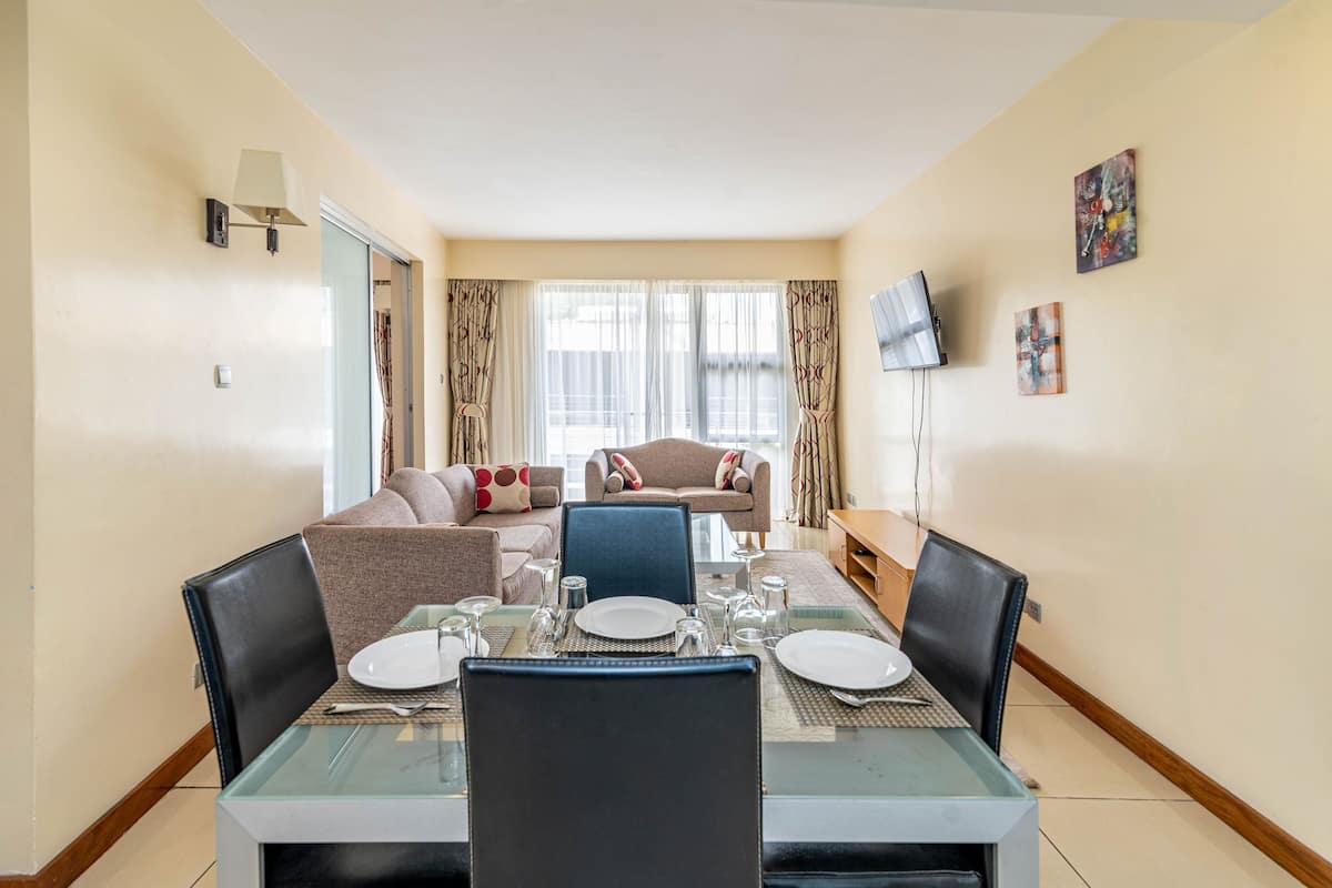 A dining area with a glass table set for four, a sofa, and a TV mounted on the wall.