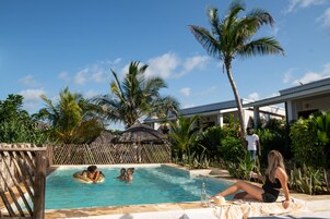 A pool area with a wooden fence, palm trees, and a thatched-roof structure.