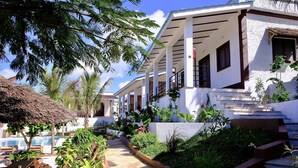 A resort with a pool, outdoor seating, and a staircase leading to a building with a white facade and brown accents. - Nyumbani Residence Apartments (Jambiani)