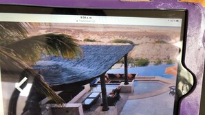 Una tableta que muestra una vista de un área de piscina con una zona de estar techada y una palmera.