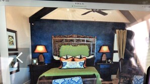 Un dormitorio con cama, dos mesitas de noche, un ventilador de techo y una ventana con cortinas.