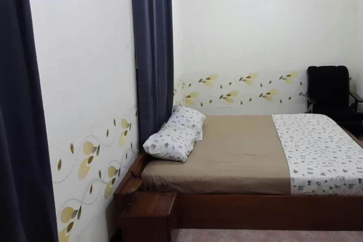 A small, single-bed room with a wooden bed frame, a headboard with a leaf pattern, a black chair, and a small wooden bench.
