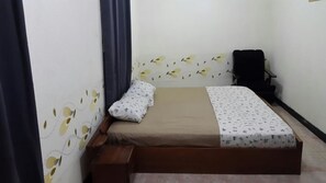 A small, single-bed room with a wooden bed frame, a headboard with a leaf pattern, a black chair, and a small wooden bench.