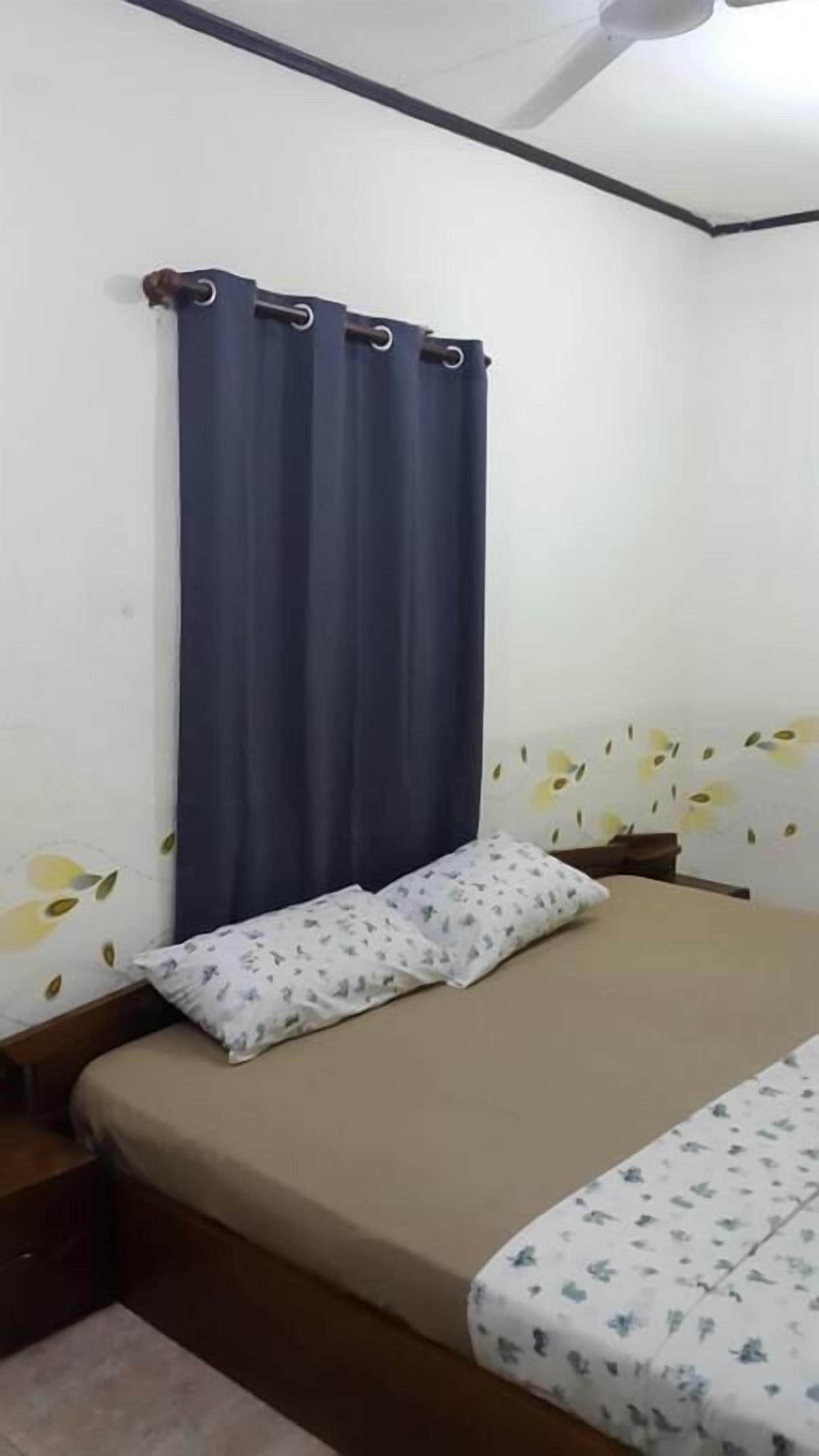 Un dormitorio con una cama, un almohadón, una cortina y una pared con estampado floral.